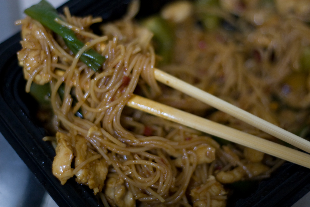 chopsticks resting in a container of noodles
