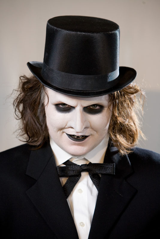 a man wearing a suit and a top hat with his hair pulled down and his face painted to look like a devil