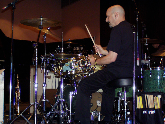 a man in black shirt sitting on top of drums in front of drum sticks