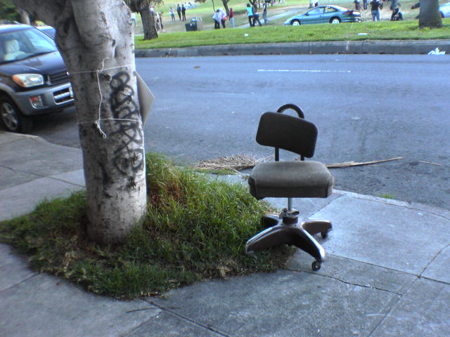 a chair sitting on a street curb next to a tree