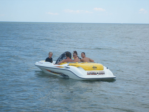 four people on the back of a white and yellow boat in the water