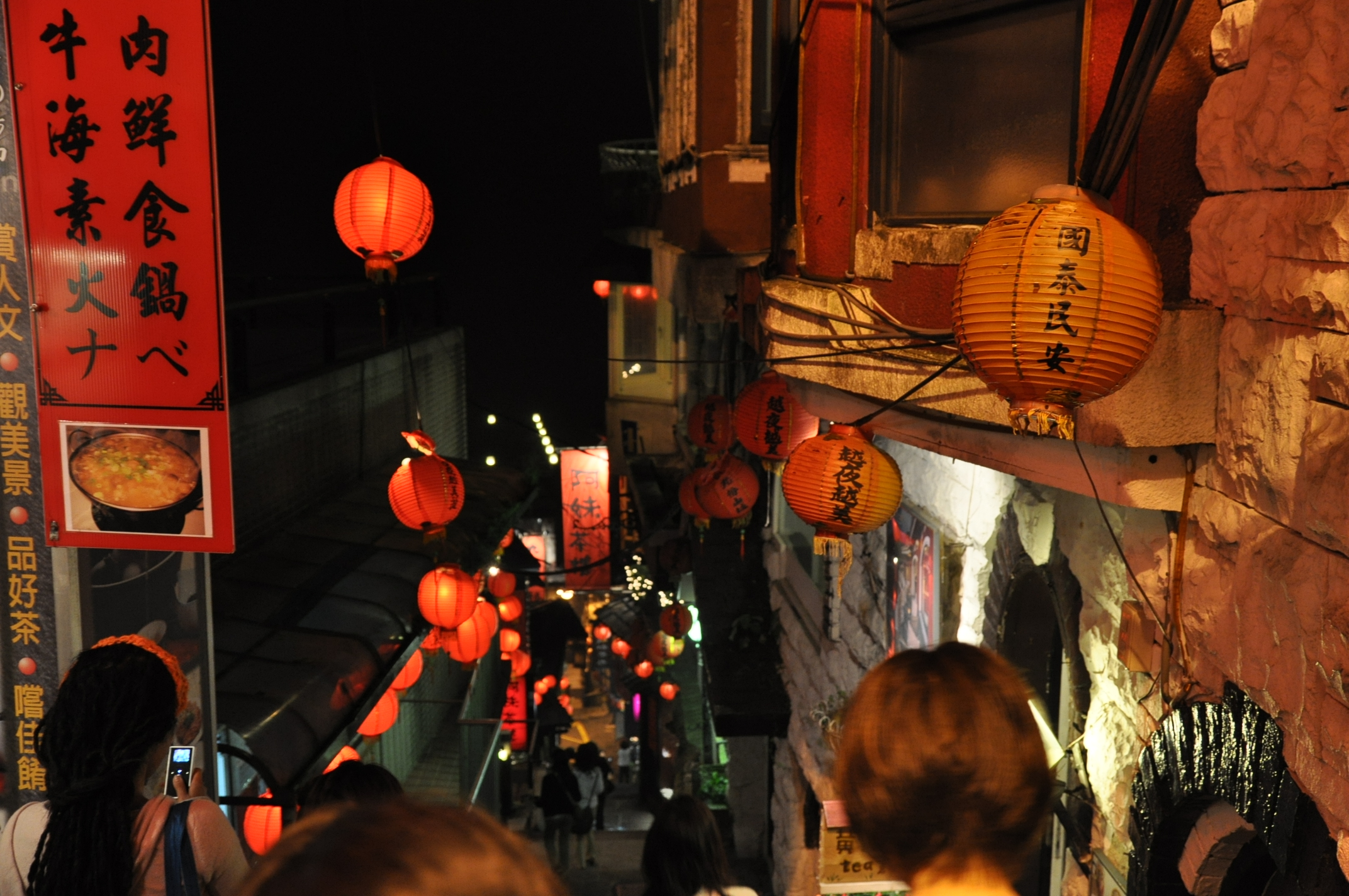 a narrow city street has oriental lanterns hanging from the building