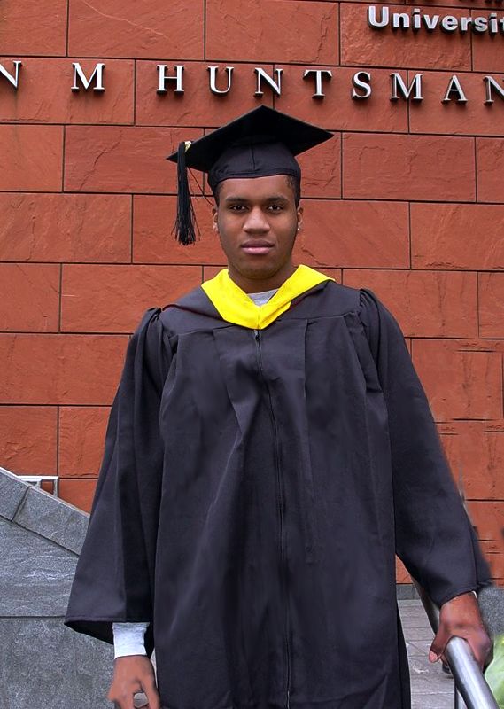 the  wearing a graduation gown stands with his hand on a cane