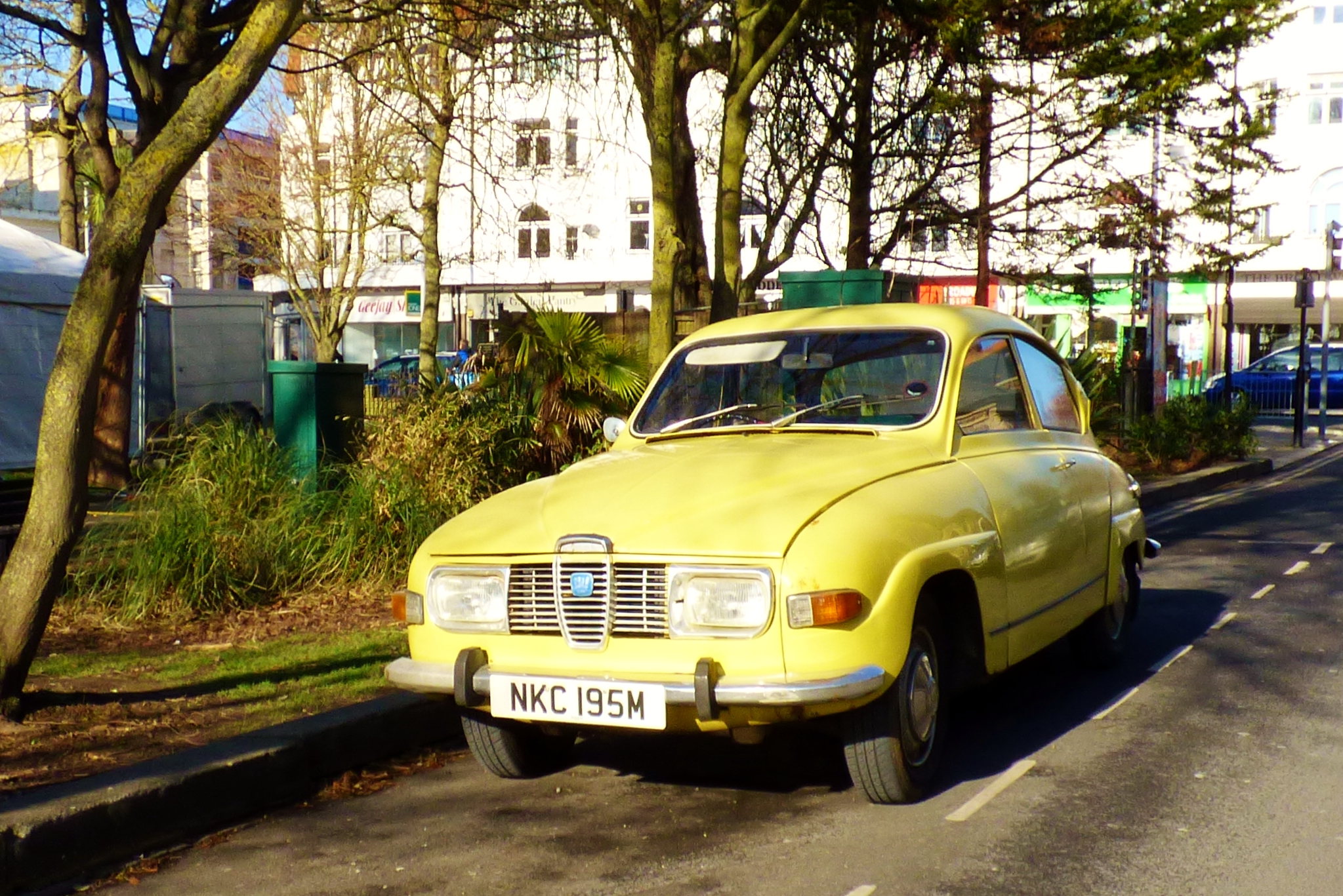 an old yellow car driving down the road