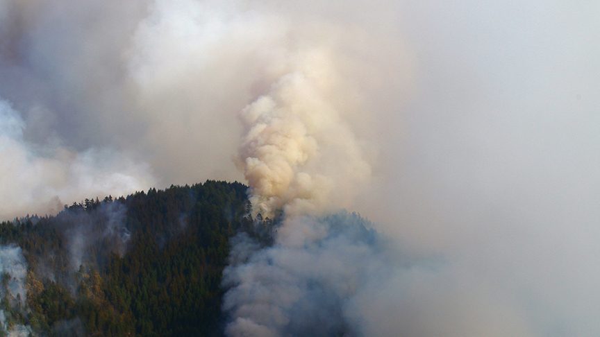 a smoke trail billows from the top of a mountain