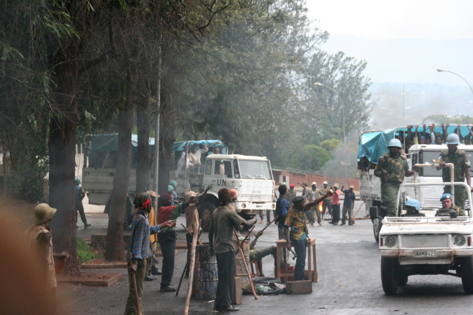 a truck carrying several objects drives down a street while people wait in line to receive soing