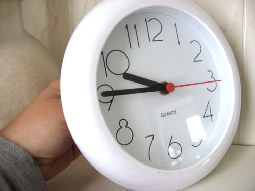 a small white clock on a wall in someones hand