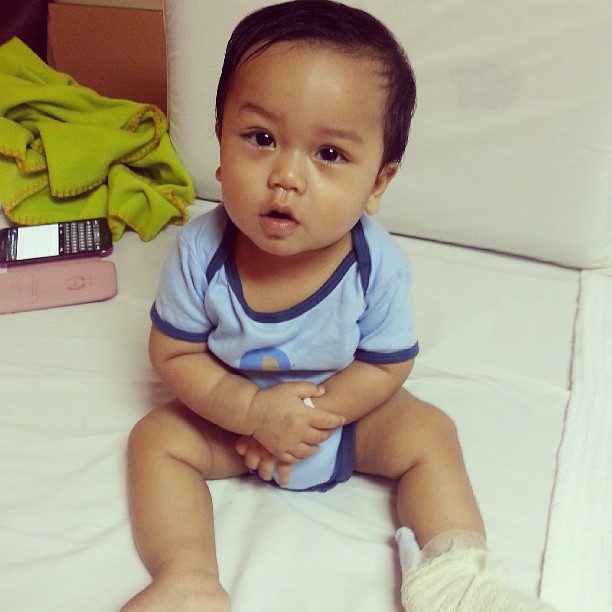 a small baby wearing a short blue shirt is sitting on a bed
