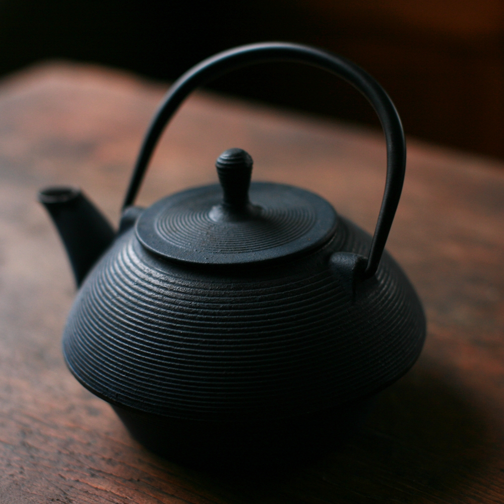 a black tea pot sitting on top of a wooden table