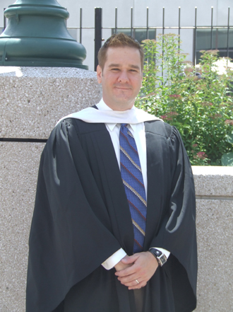 a man in a graduation gown and a robe standing next to a light