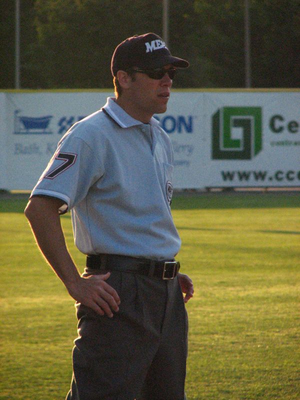 a man stands on a baseball field wearing glasses and a hat