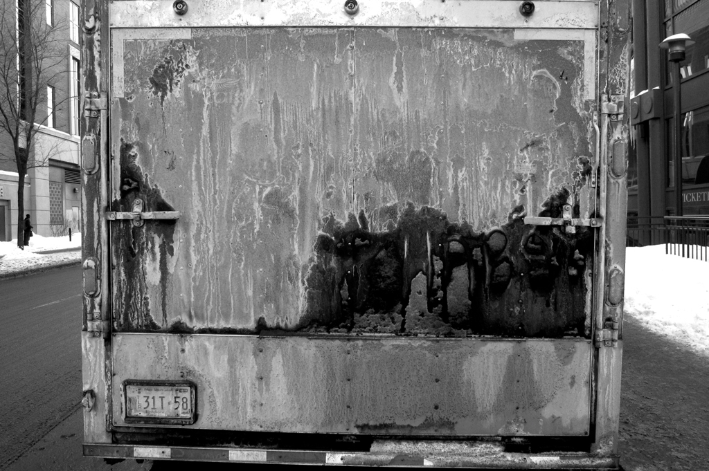 the back end of an old rusty truck on a snowy street