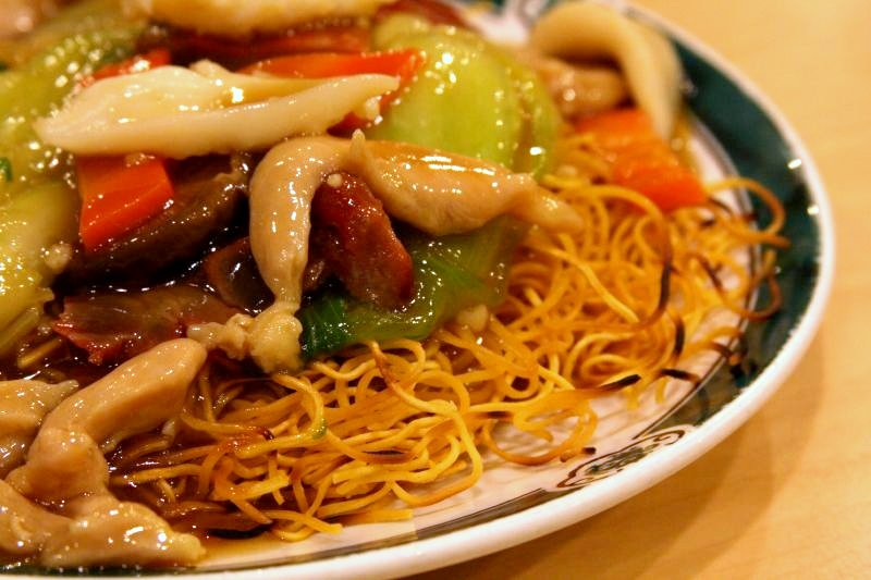stir fry chicken with noodles and vegetables is sitting on a green and white plate