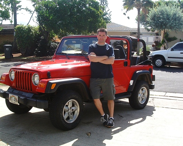 man standing next to a red jeep with arms crossed