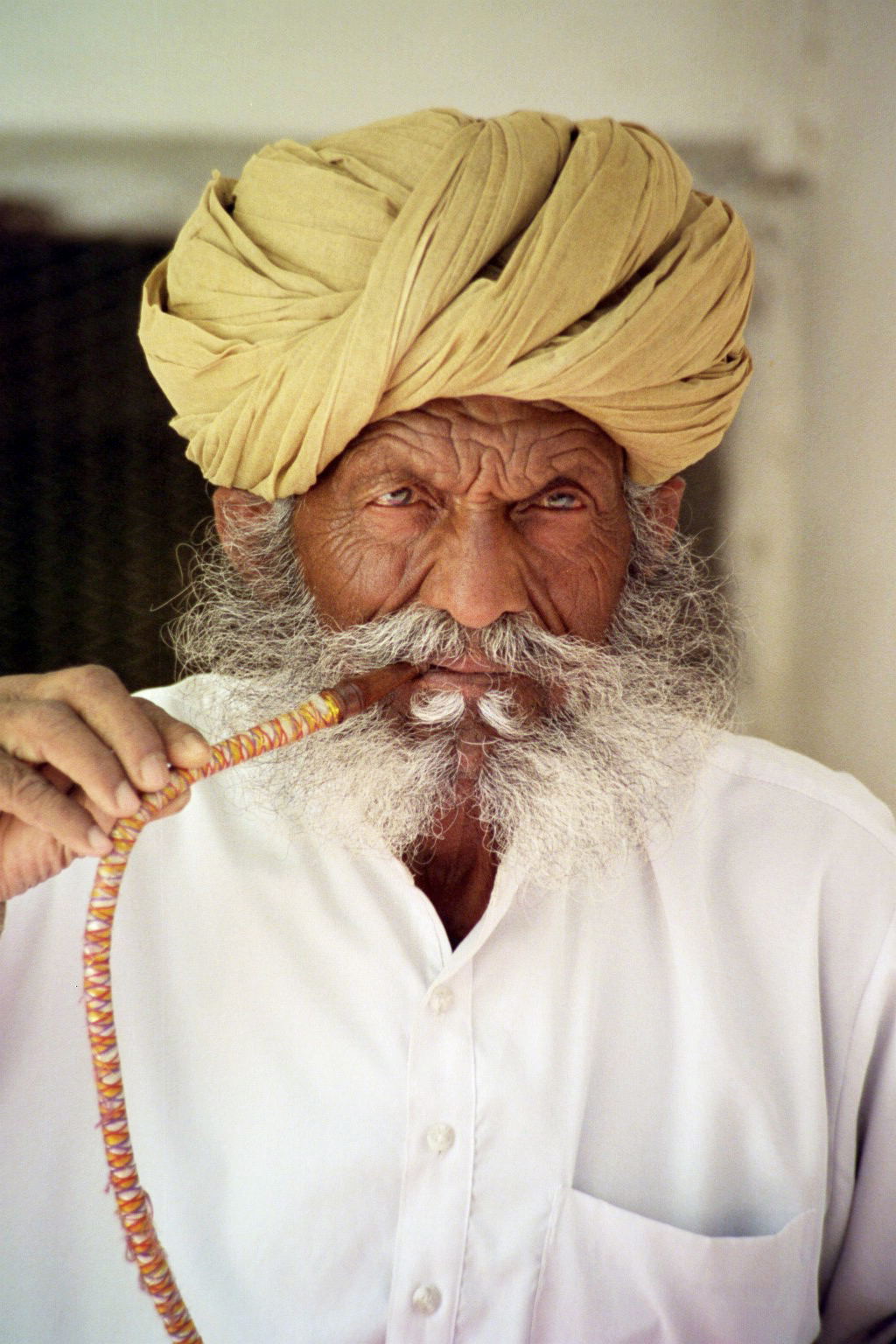 a man with a long grey beard is dressed in yellow turban and talks on a phone