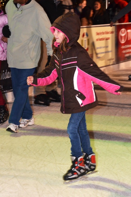 a little girl is wearing a pink hat and holding her hand while ice skating
