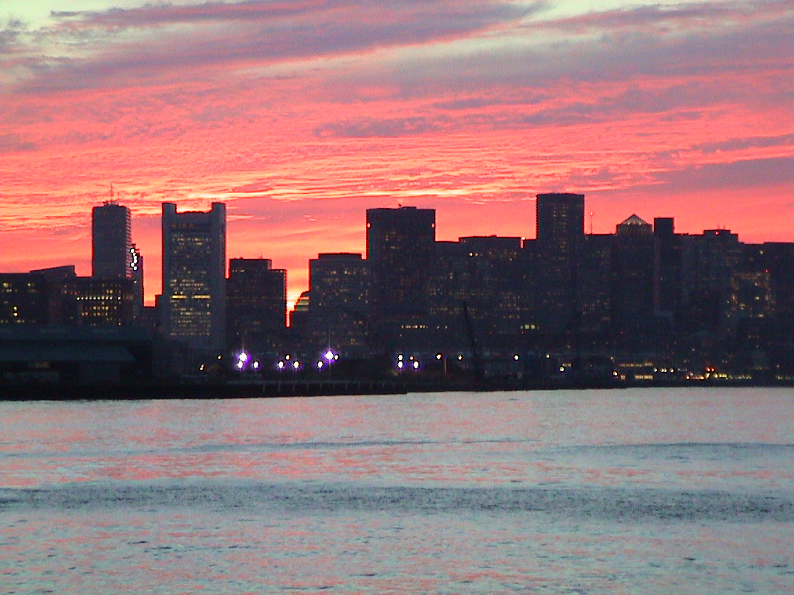 the skyline is silhouetted against a pink sunset over the water