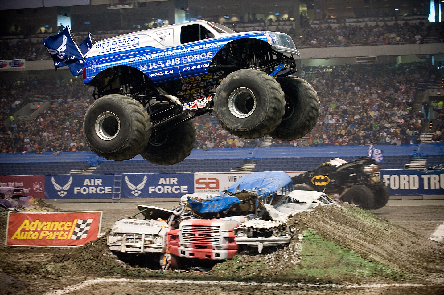 a blue truck is in the air and it has four huge tires in front of it