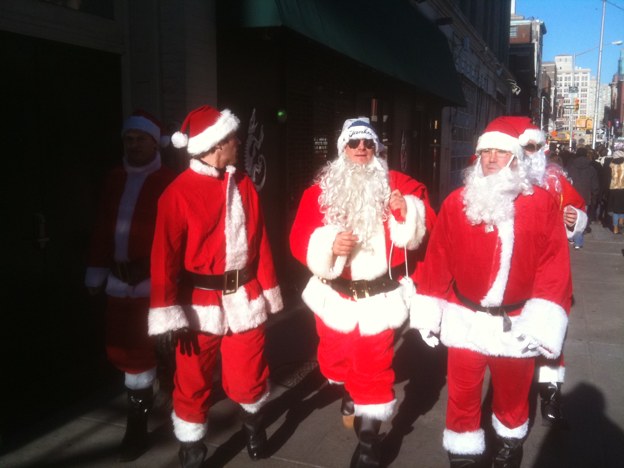 three santas walking down a street with bags