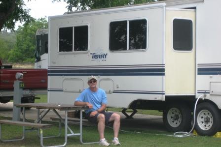 a man sits at a table with an rv behind him