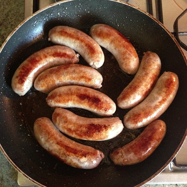 many sausages are cooking in a frying pan on a stove top