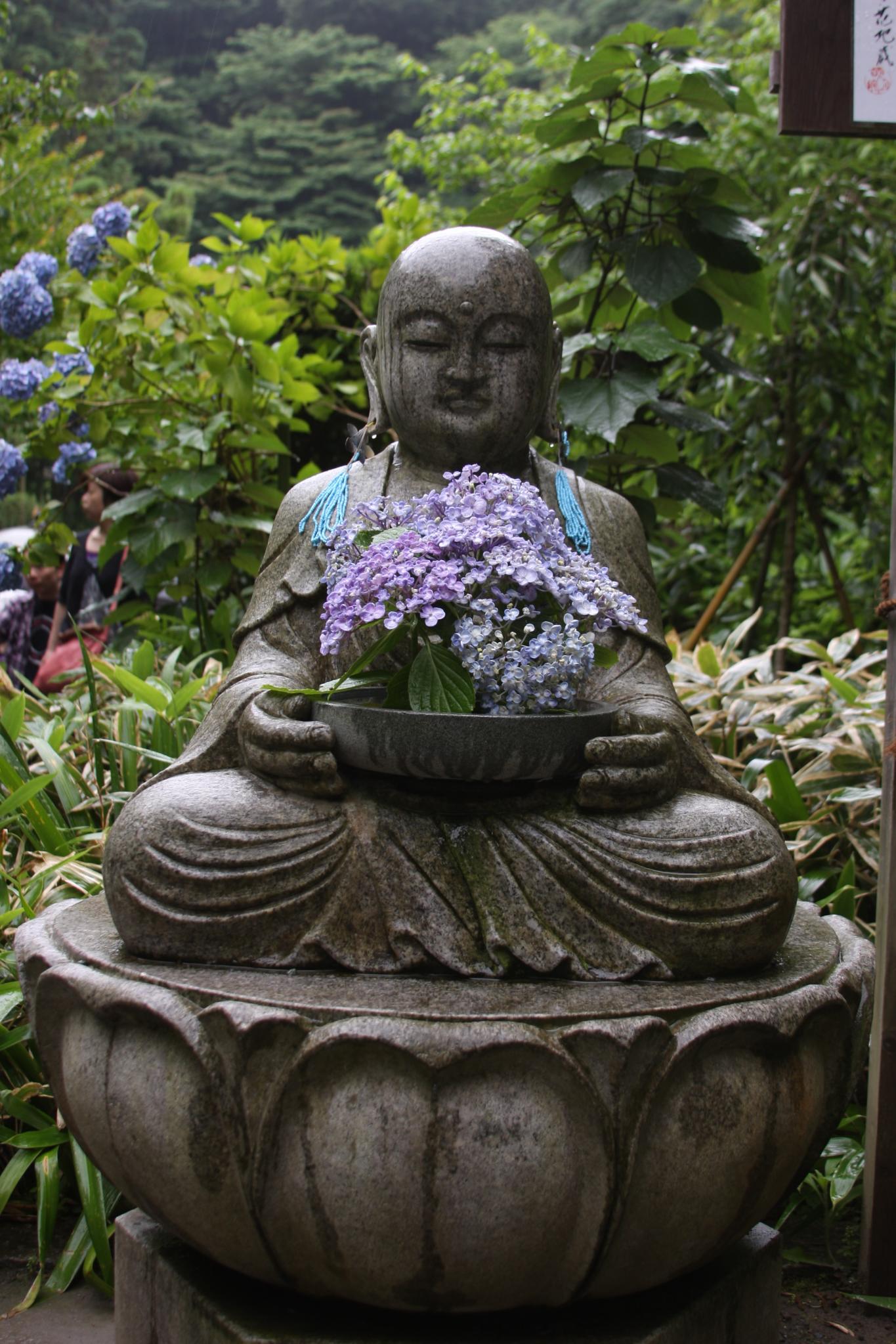 a buddha statue with flowers sitting on the edge of it