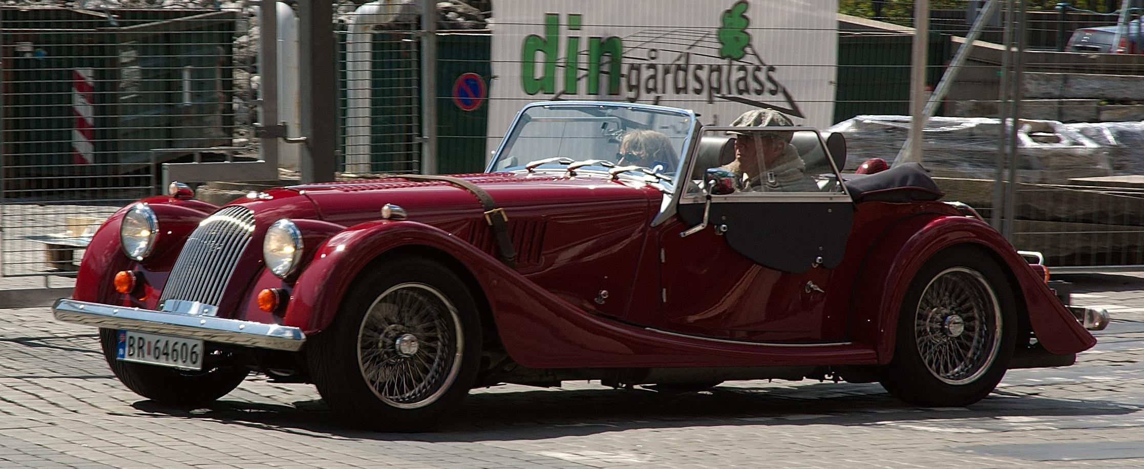 a red classic car is driving down the road