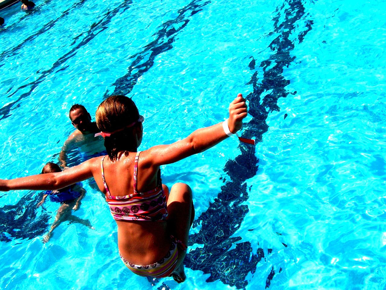 a girl is floating in the pool and reaching her arm out to catch the ball