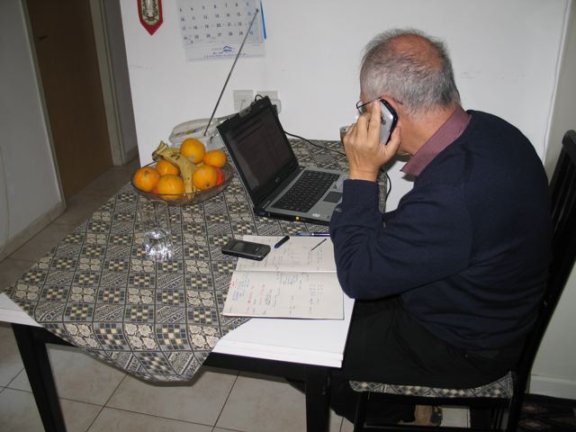 the old man is on his laptop while talking on a phone
