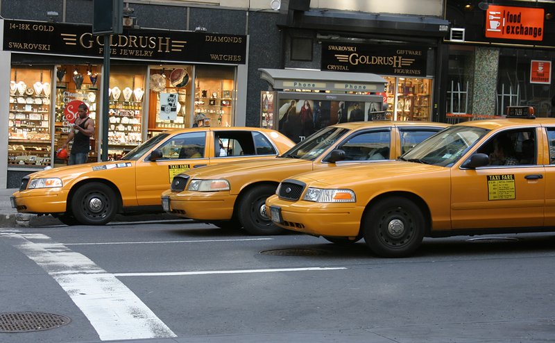several taxi cabs sit at an intersection on a city street