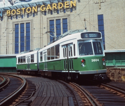 green and white electric trolley on railroad tracks with a historic building in the background