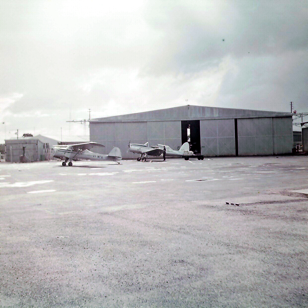 several planes sit on a small runway near large hangars