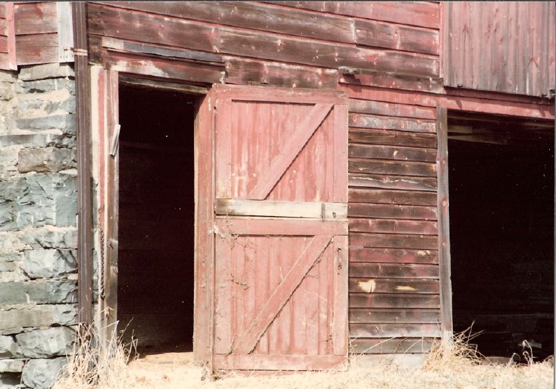 two open red doors are on an old red barn