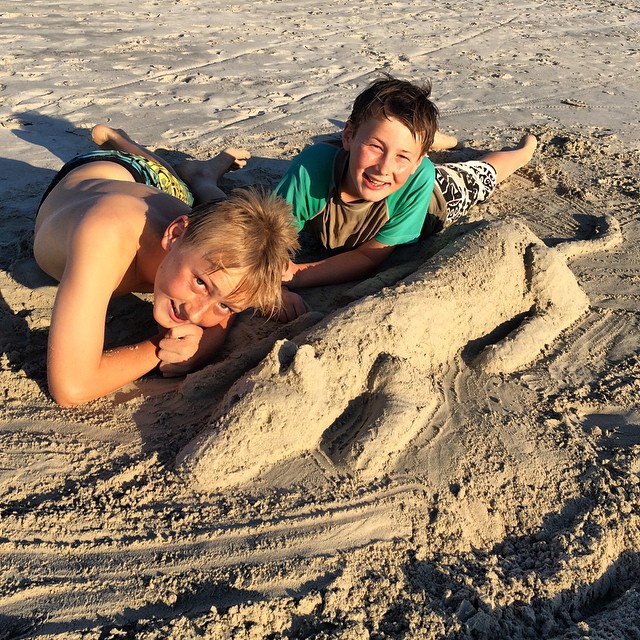 two children laying on a sandy surface with sand sculptures