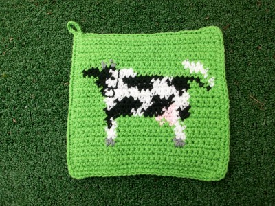 a green crocheted bag with white and black cow on it