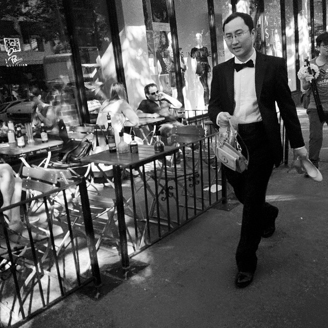 a man wearing a tuxedo walking down the street in front of a cafe