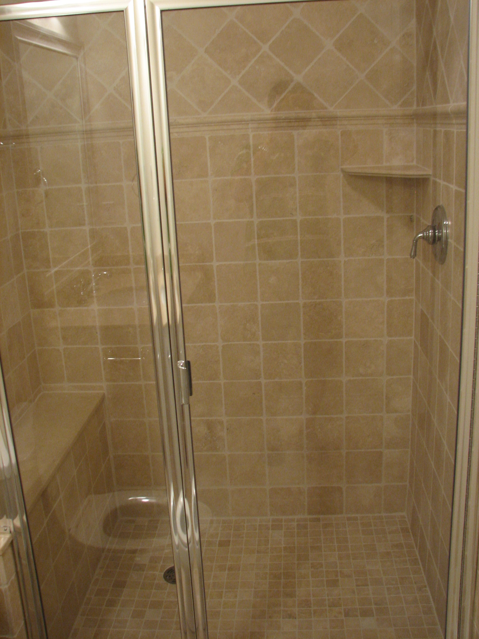 a glass shower door in a tan tiled bathroom