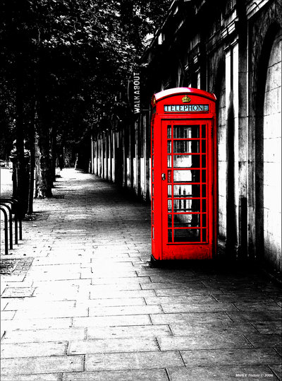 a red telephone booth is located beside a sidewalk