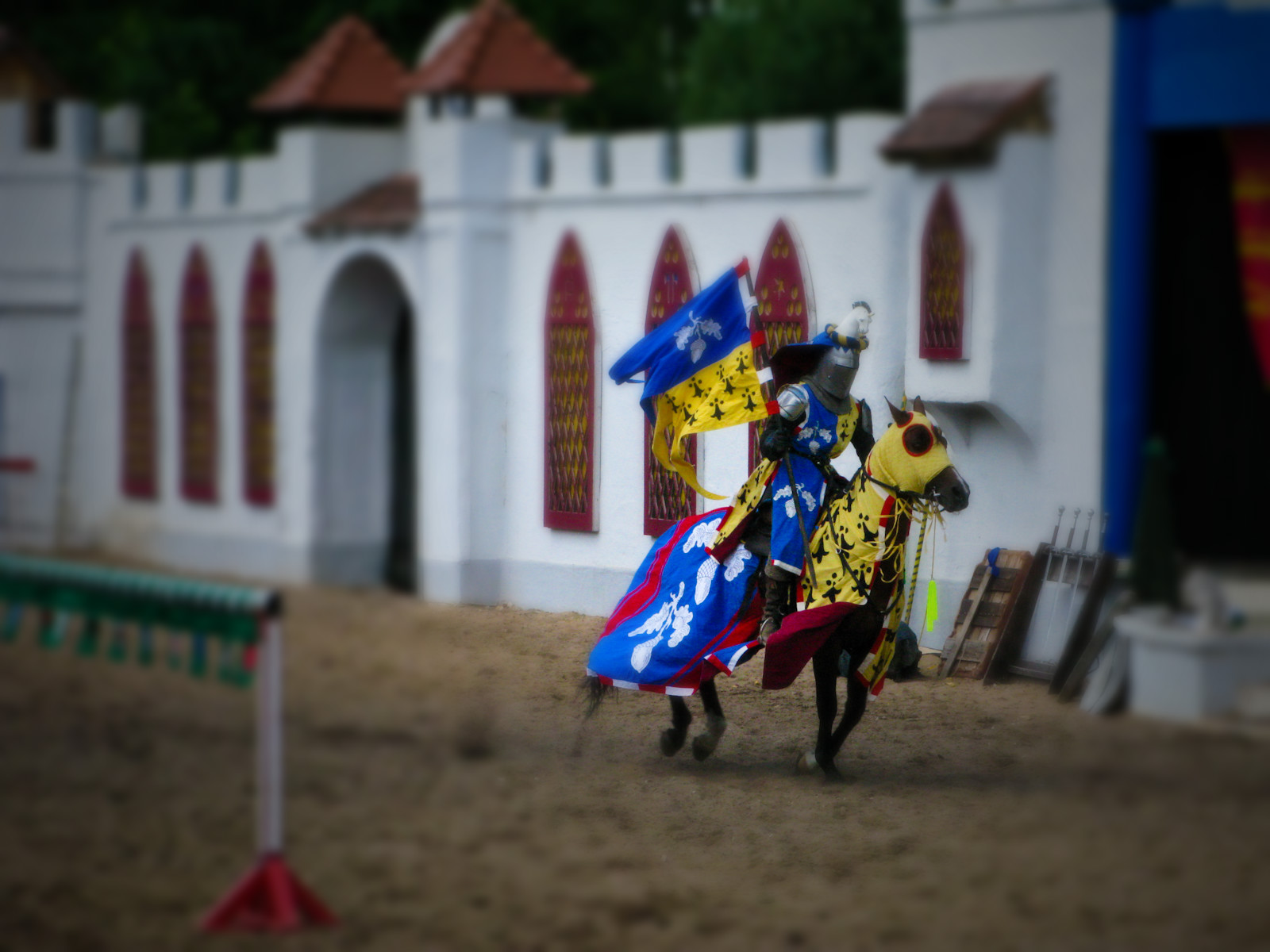 two men riding horses holding colorful flags on a dirt ground