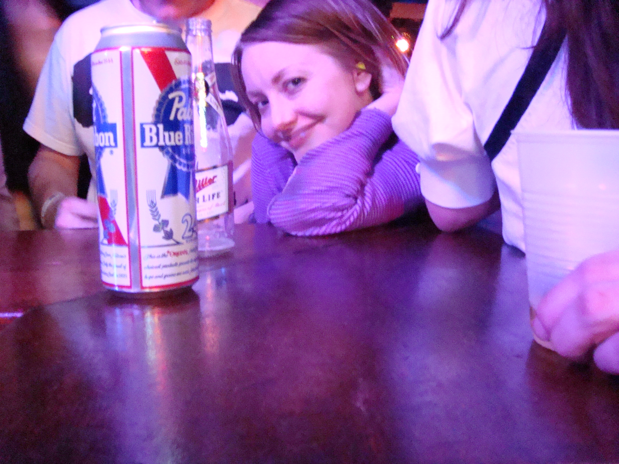 a smiling girl leaning on a beer can in front of other people