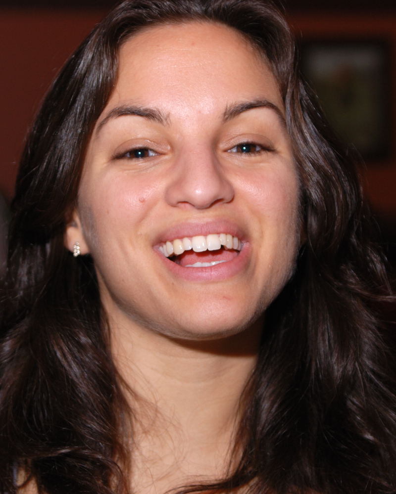 a smiling woman with large hoop earrings next to a white pizza