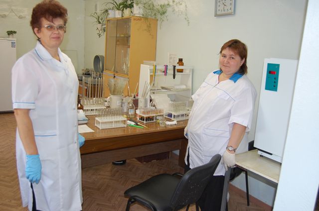 a couple of women in lab coats standing next to a table