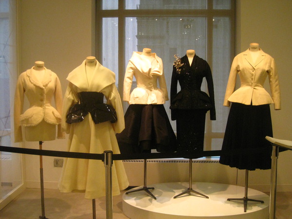 various white dresses are displayed on stands in front of a window