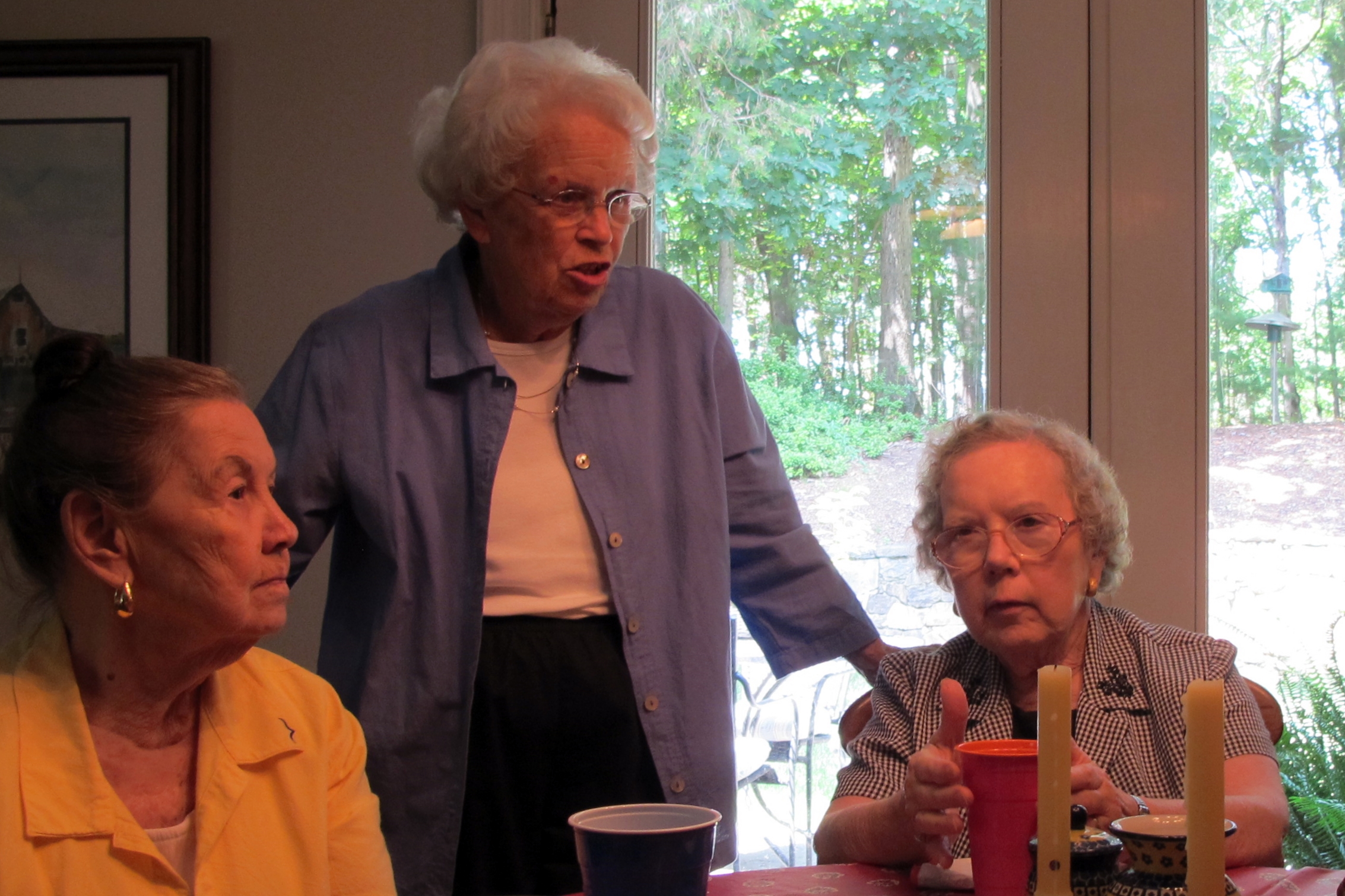 a woman holds her hands on her chest while standing next to other women in front of a table and looking down at a candle