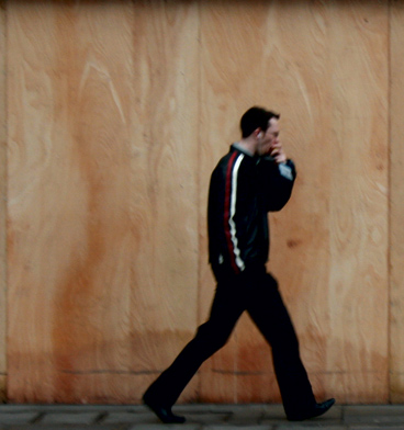man walking on sidewalk while talking on cell phone