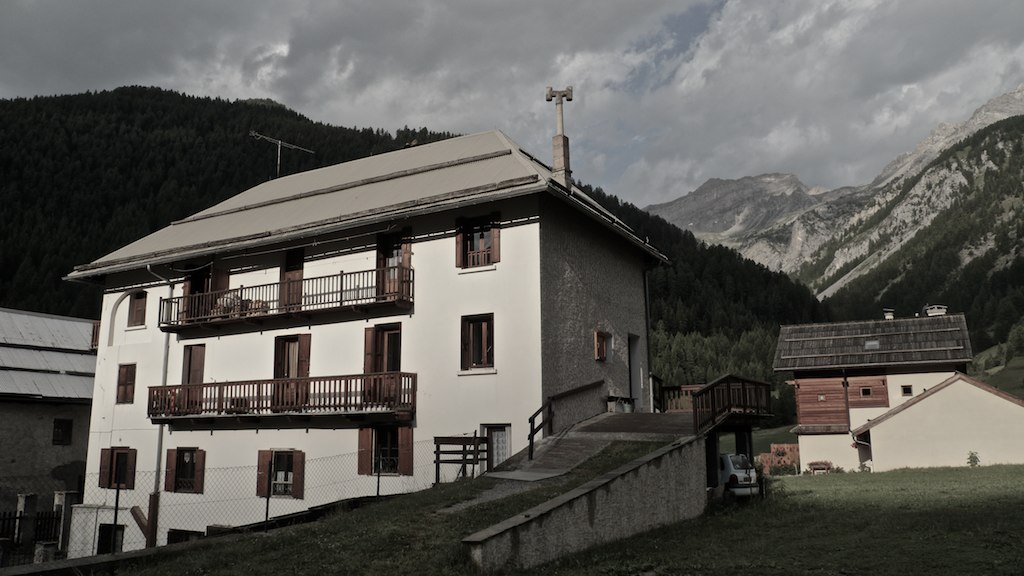 a building with balconyes sits on the top of a grassy hill near a village