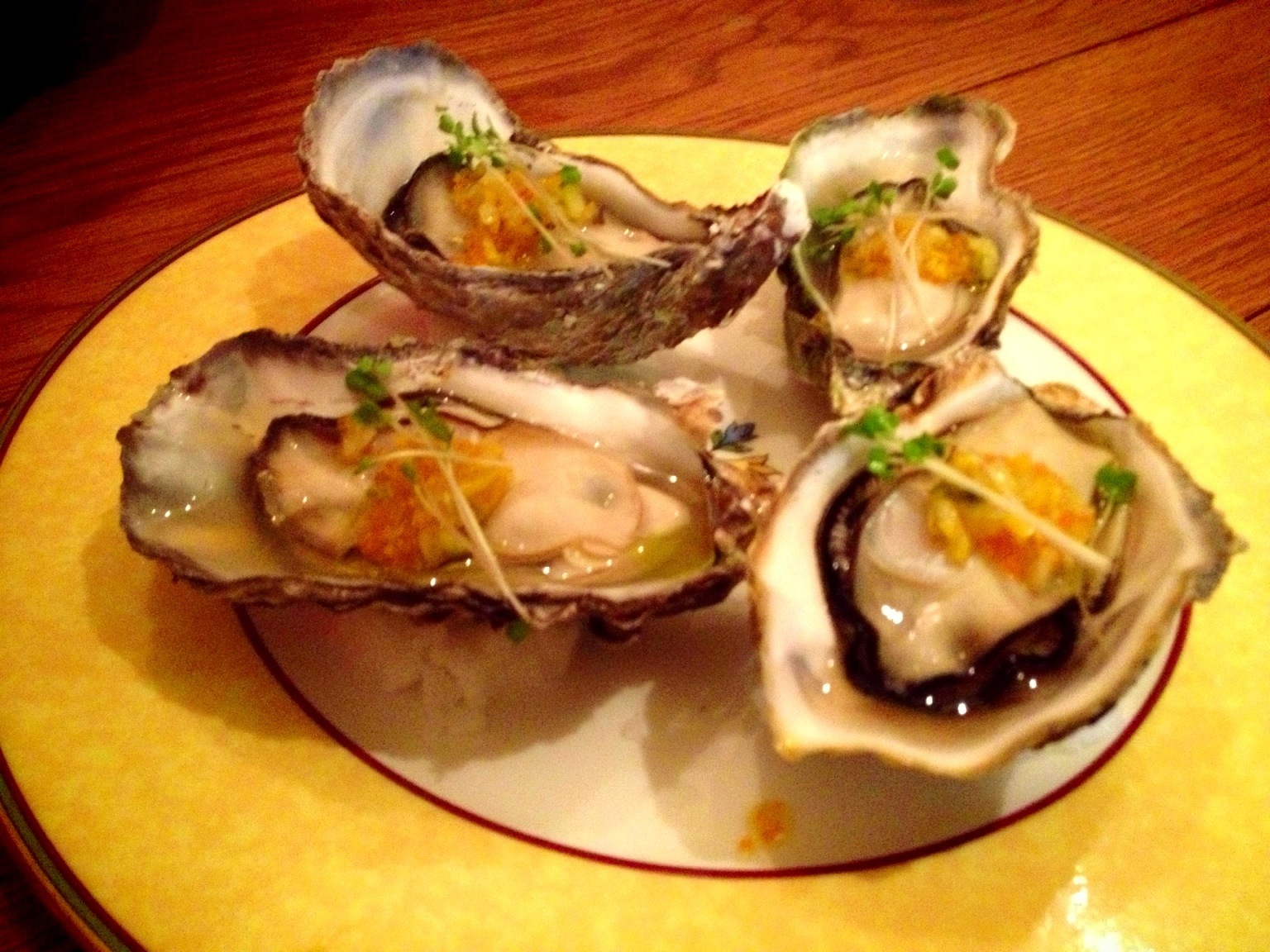 five oysters on an oval plate sitting on a wooden table
