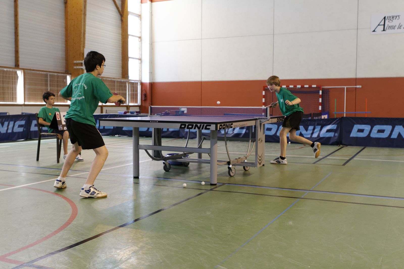 children playing ping pong in a gym, wearing green shirts