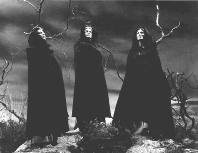 three witches posing for the camera, with one staring directly into the camera