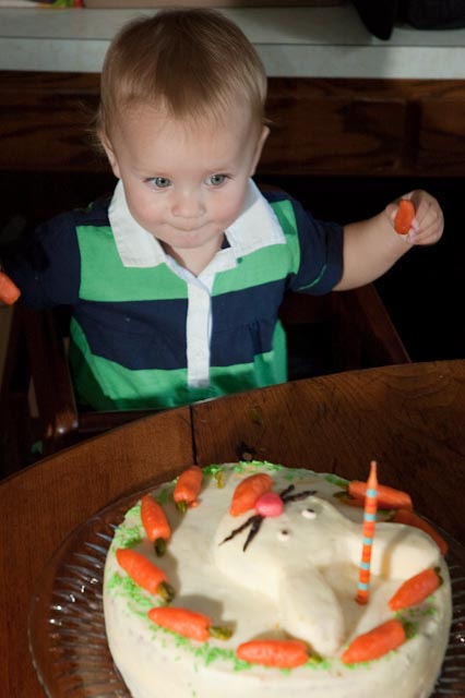 a young child standing in front of a carrot shaped cake